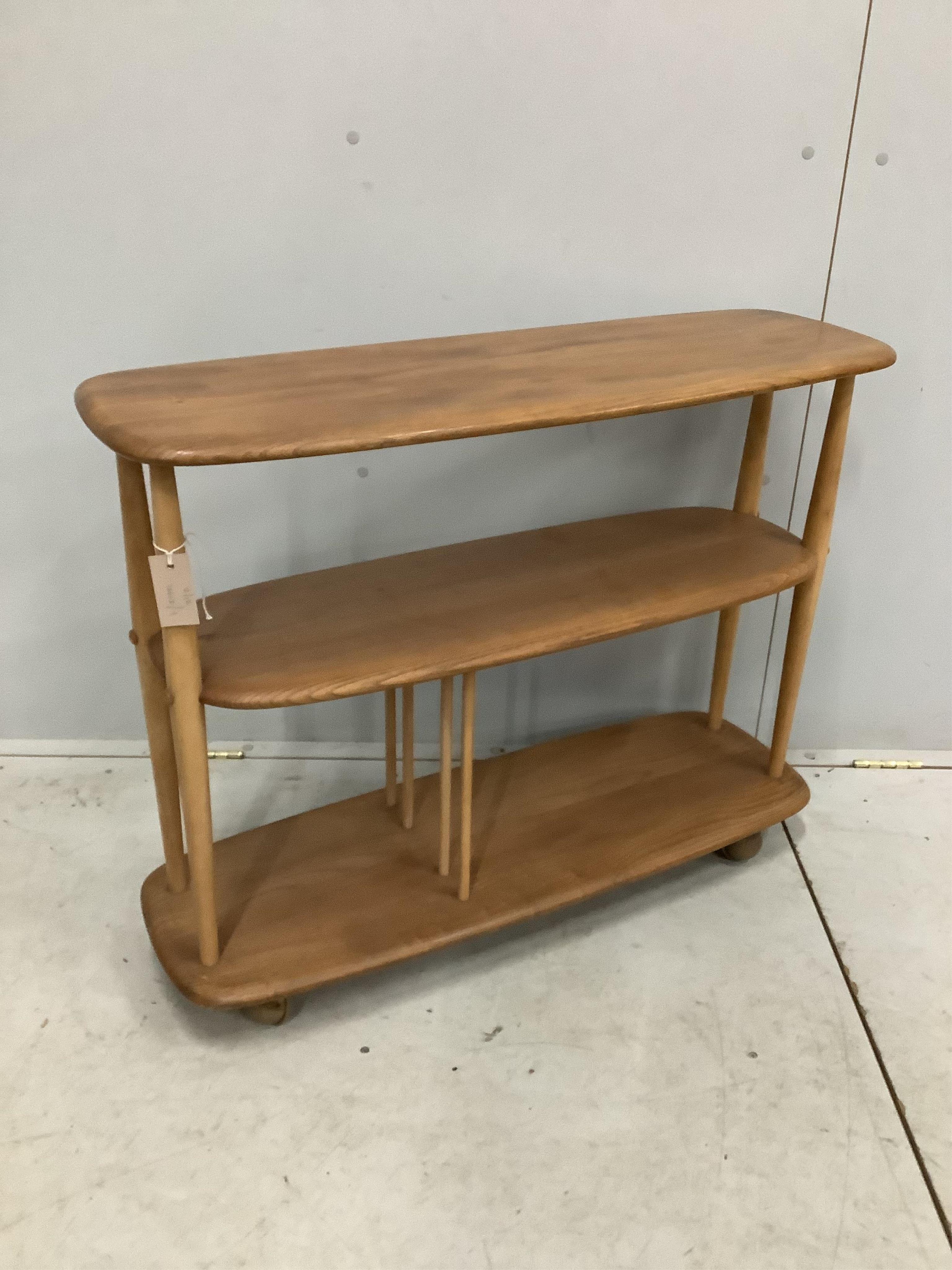 An Ercol Windsor elm and beech three tier book trolley, model 361. Width 91cm, depth 32cm, height 71cm. Condition fair to good, a little sun faded.